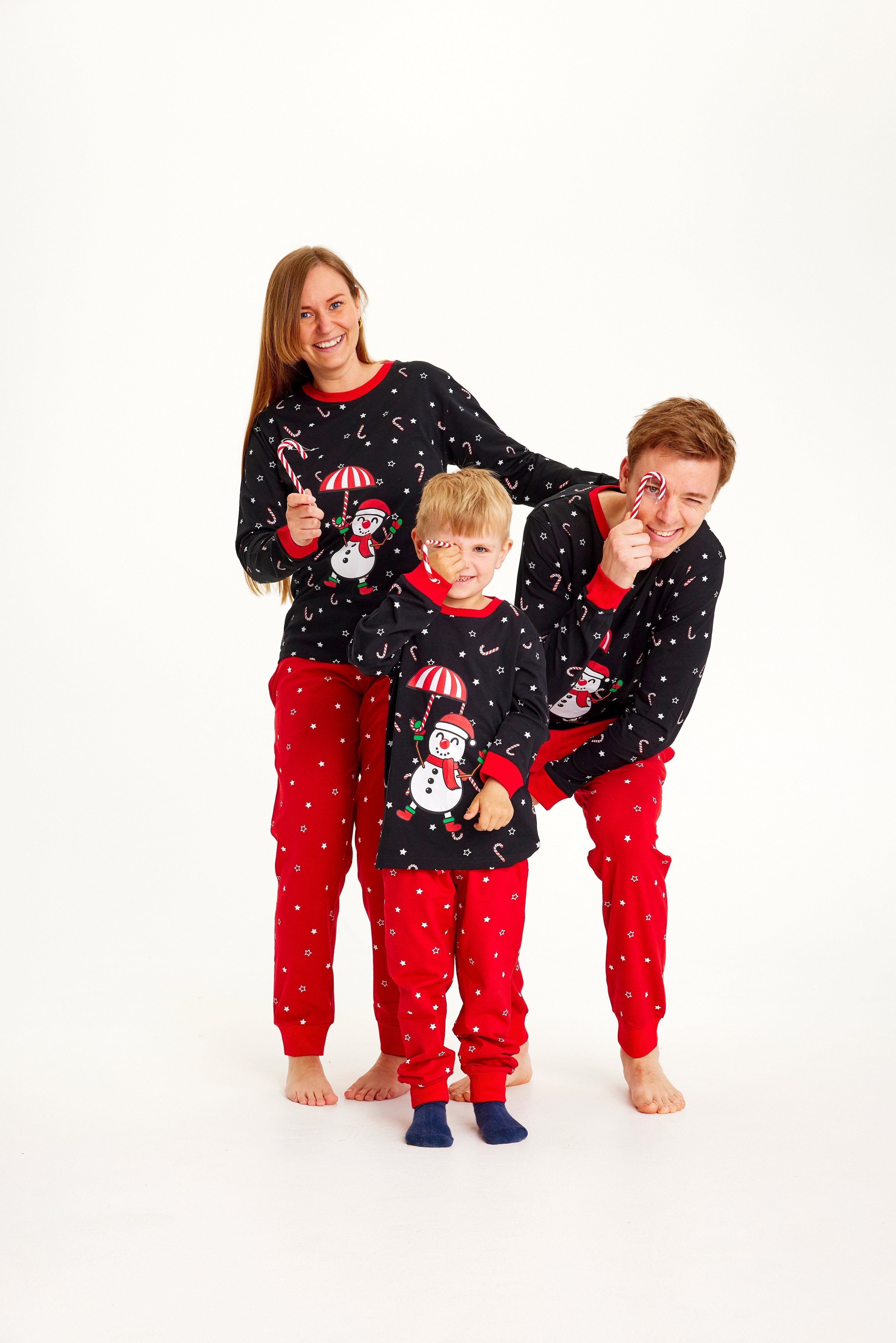 Une famille posant ensemble en pyjama de Noël noir et rouge avec un bonhomme de neige.